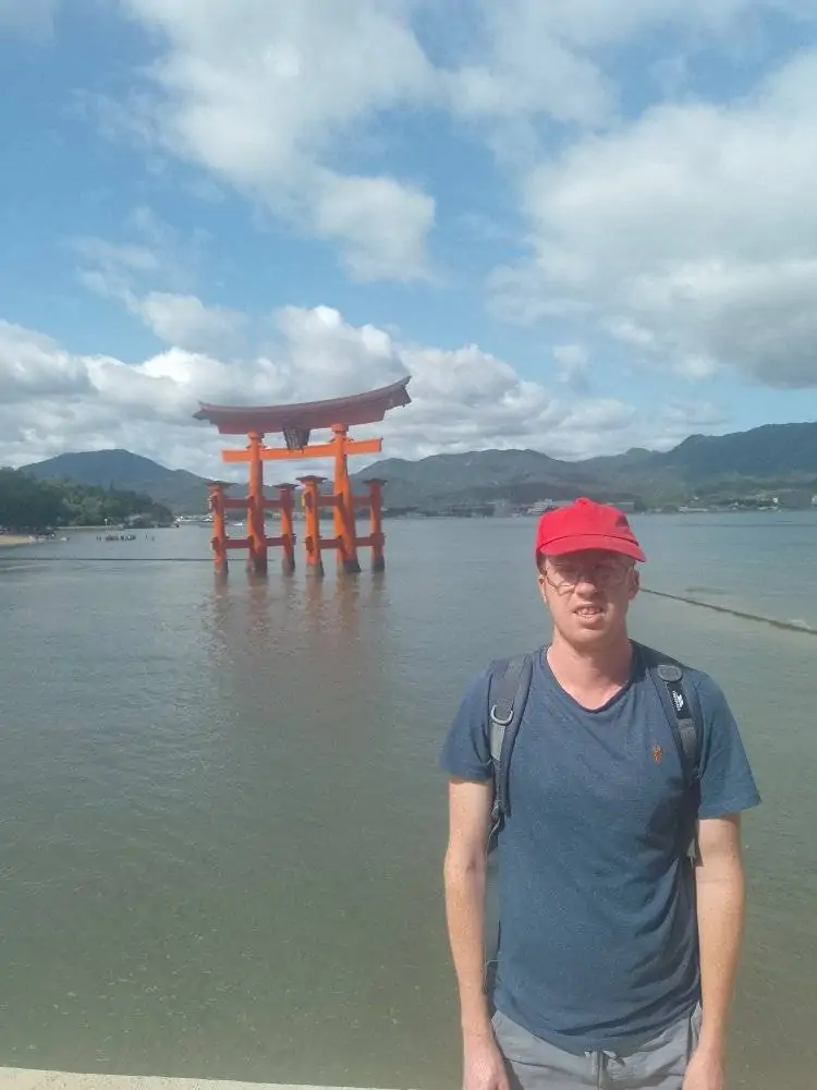 Itsukushima Shrine 'floating' in the sea with the city and hills behind.